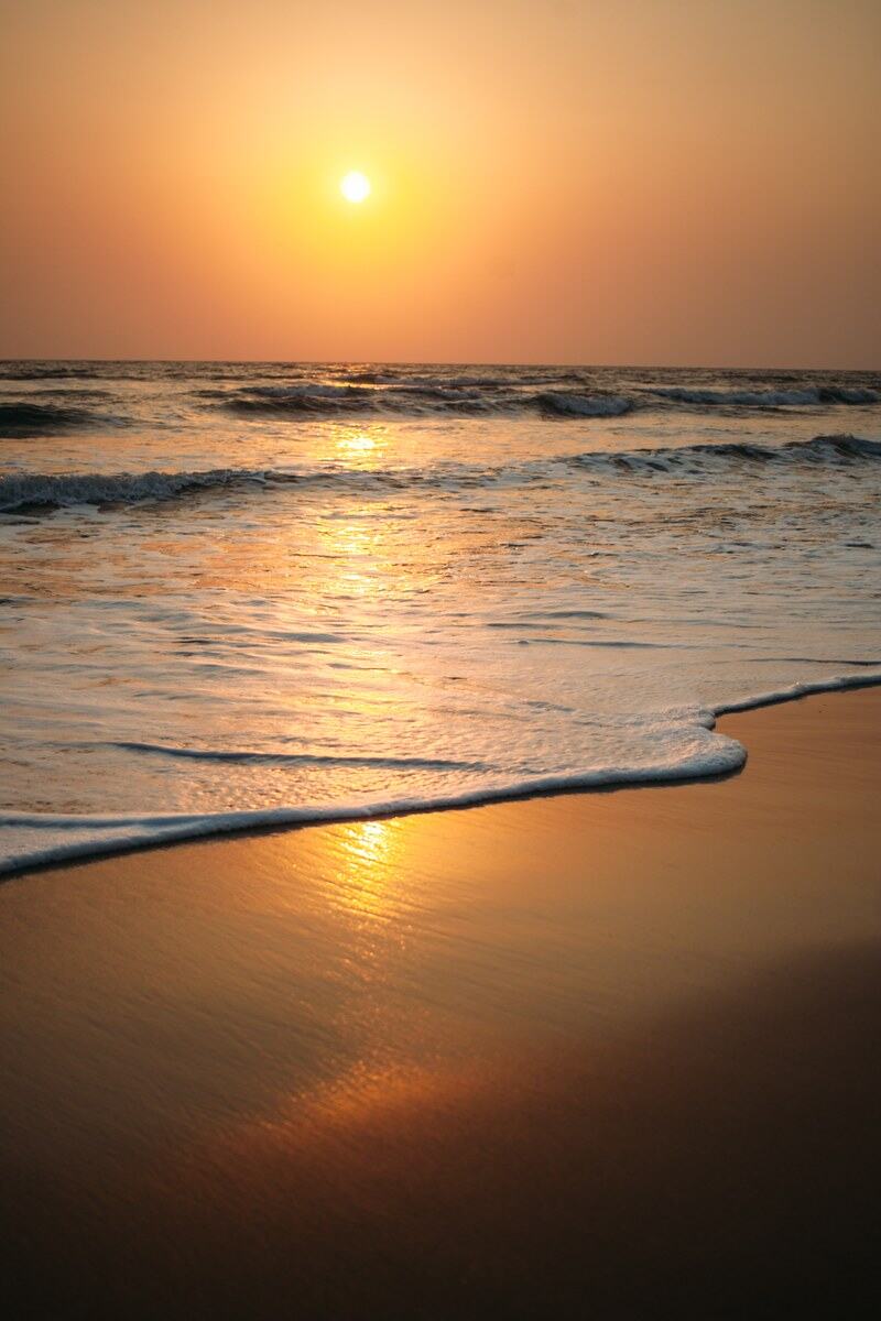 Foam curls up a Goa beach in warm sunset light.