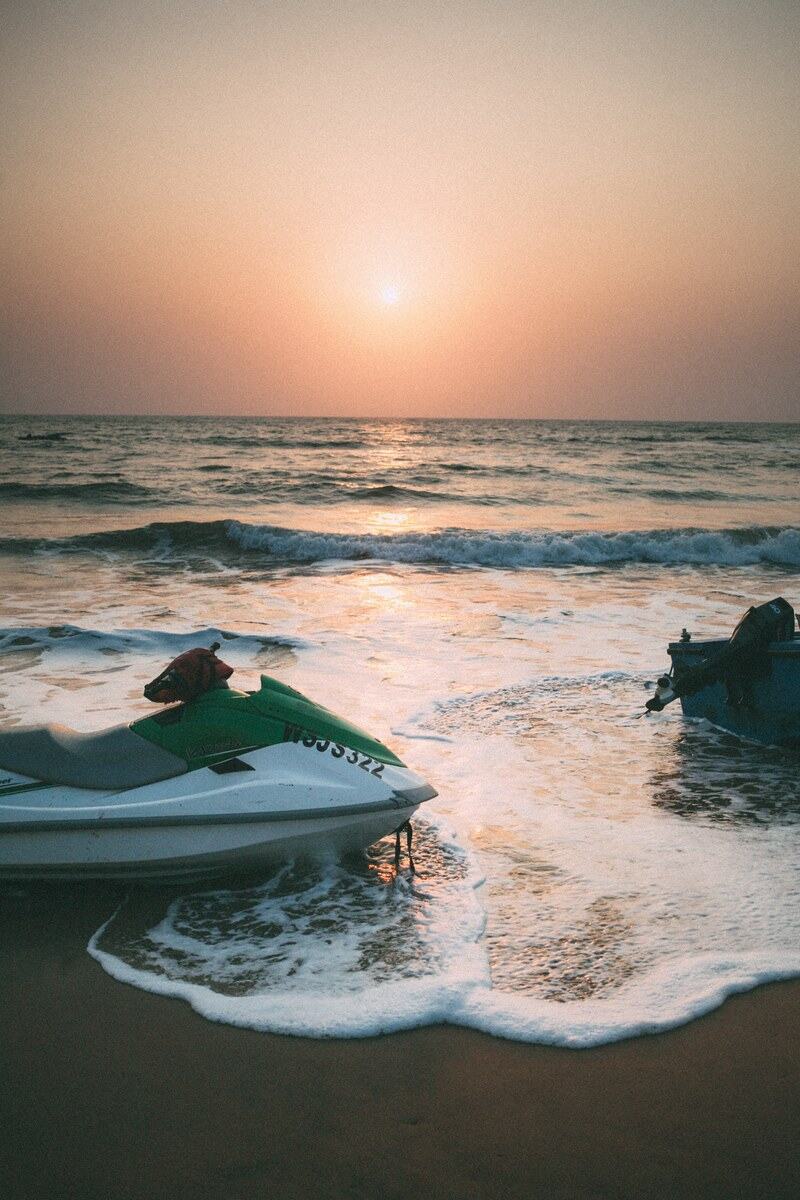 Watercraft rest in the Goa surf at sunset.