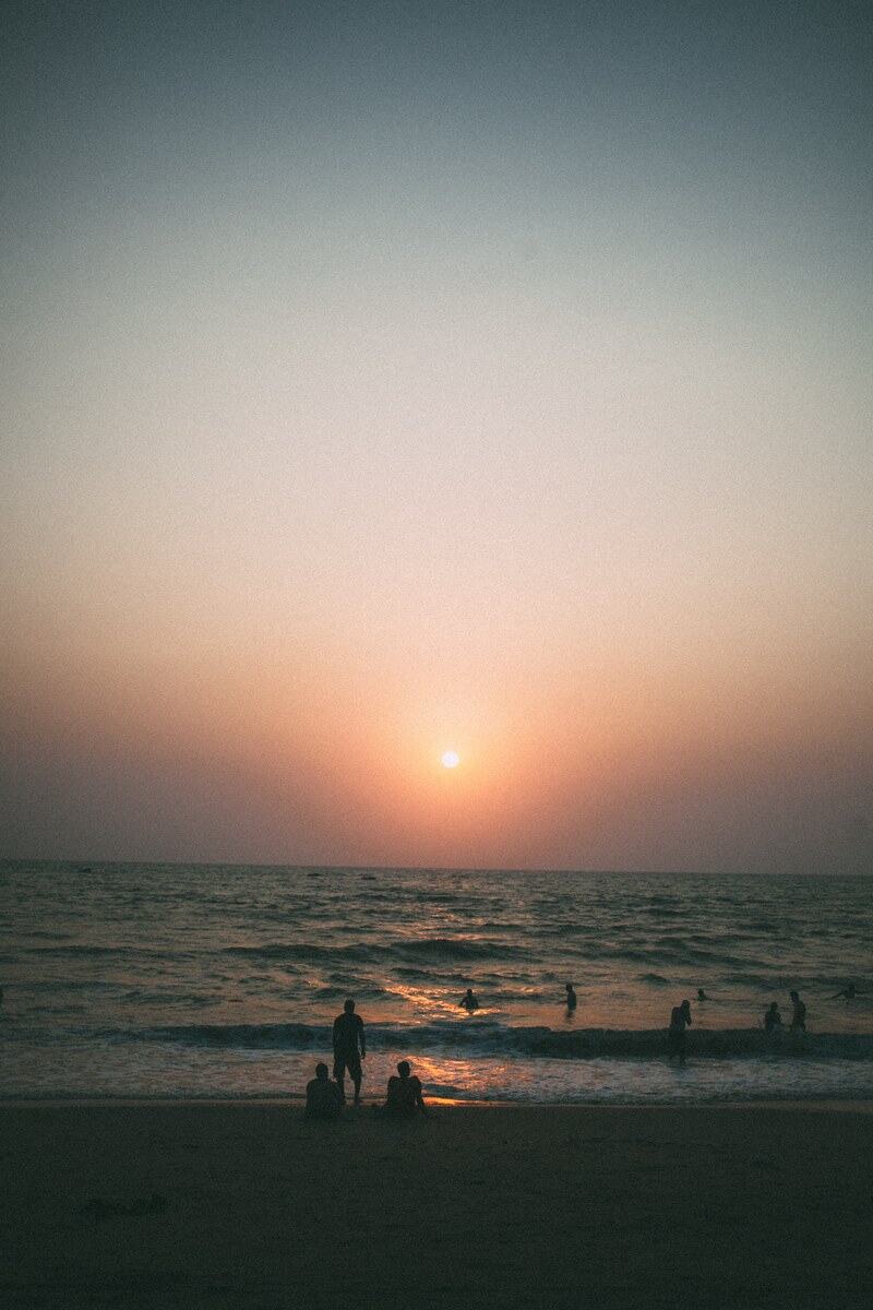 A quiet Goa beach sunset with people small against the water.