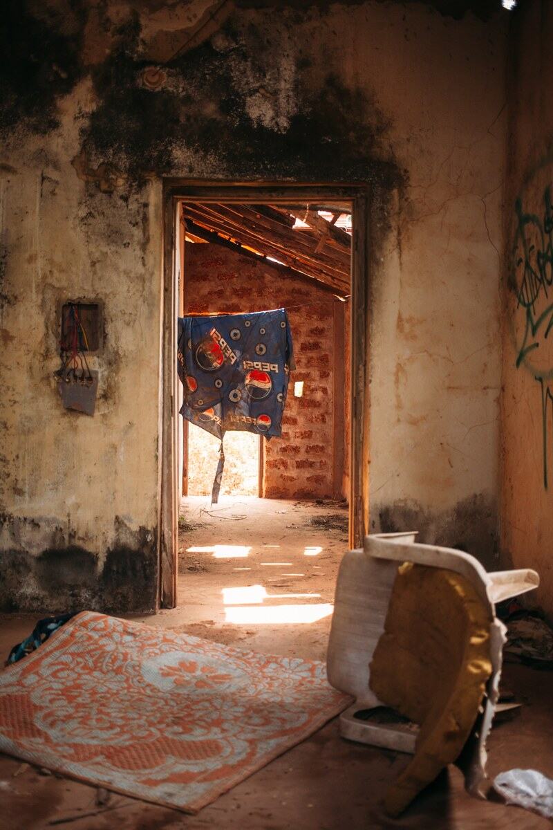 An abandoned Goa house interior opens to a bright doorway and weathered walls.