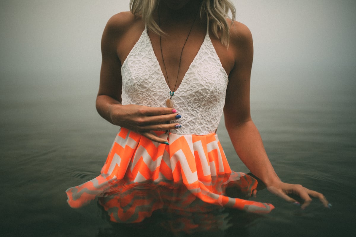 A seated figure in white and orange at Okanagan Lake in Kelowna, with forest-fire smoke turning the lake air pale and stark.