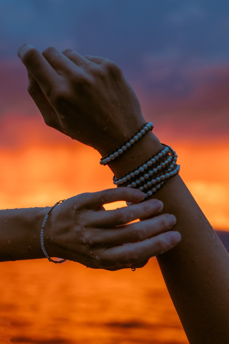 Hands and bracelets catch a stunning orange sunset over Okanagan Lake at Bertram Park in Kelowna.