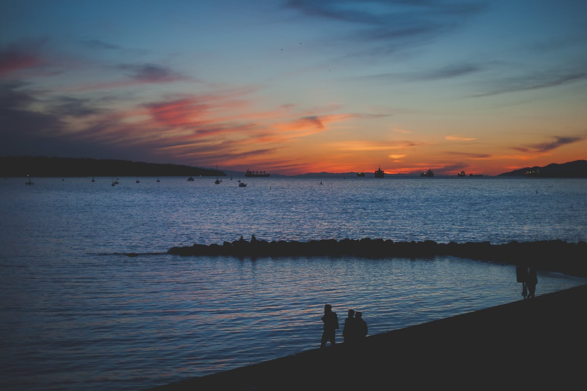 Blue and rose sunset colour over English Bay with tiny figures on the shore.
