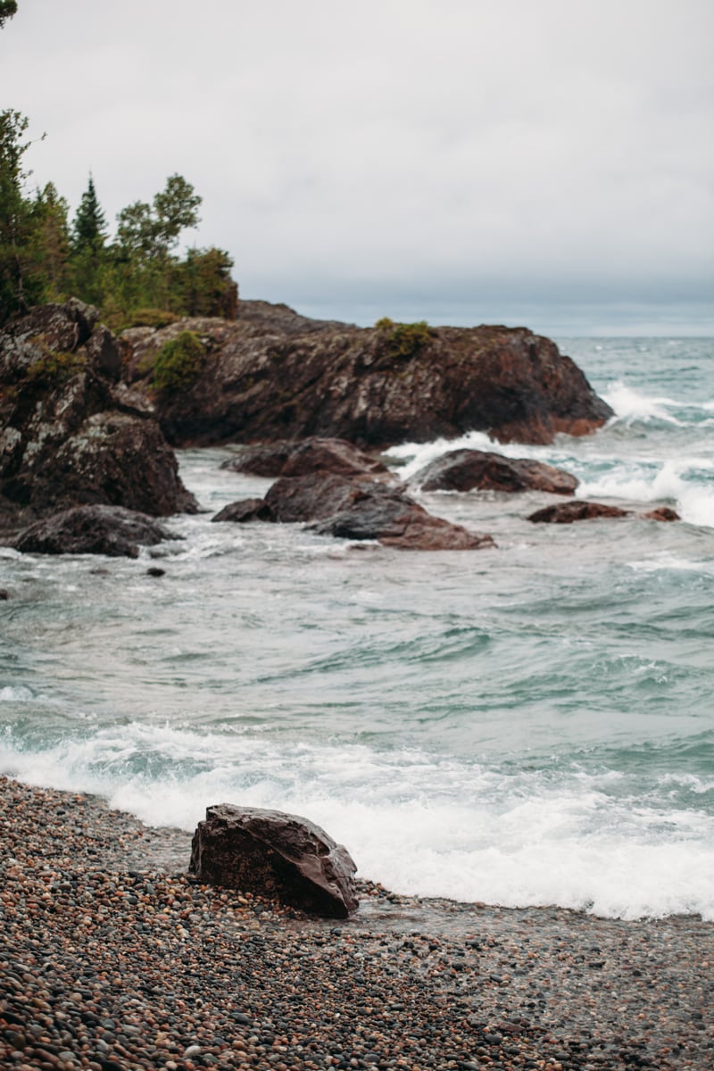Lake Huron waves break around a dark rock shelf and forested edge.