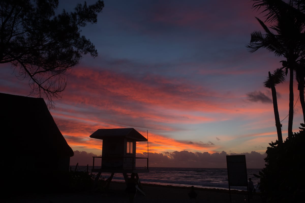 A Miami beach lifeguard hut silhouetted against red-purple sunset.