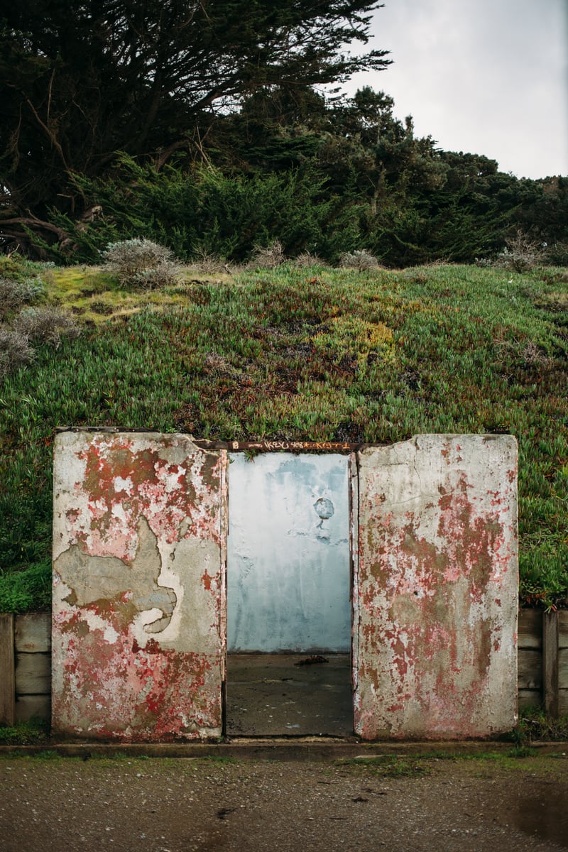 Weathered doors, painted metal and old military concrete near Baker Beach, where nature starts reclaiming the wall.