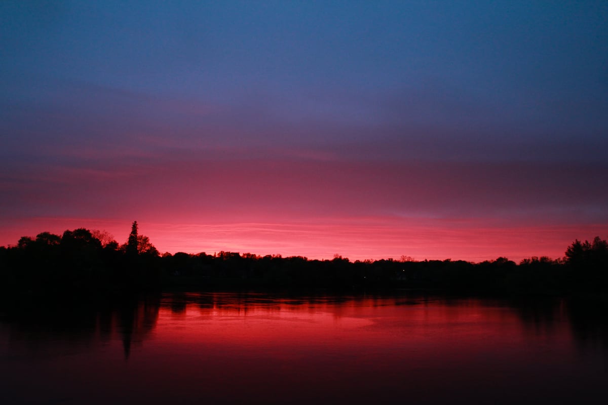 A magenta lake sunset reflects against a dark Peterborough tree line.