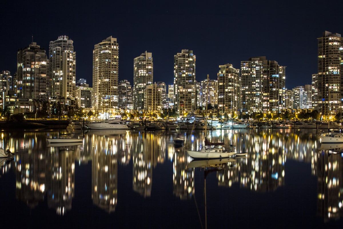 Vancouver towers reflect in black water at night.