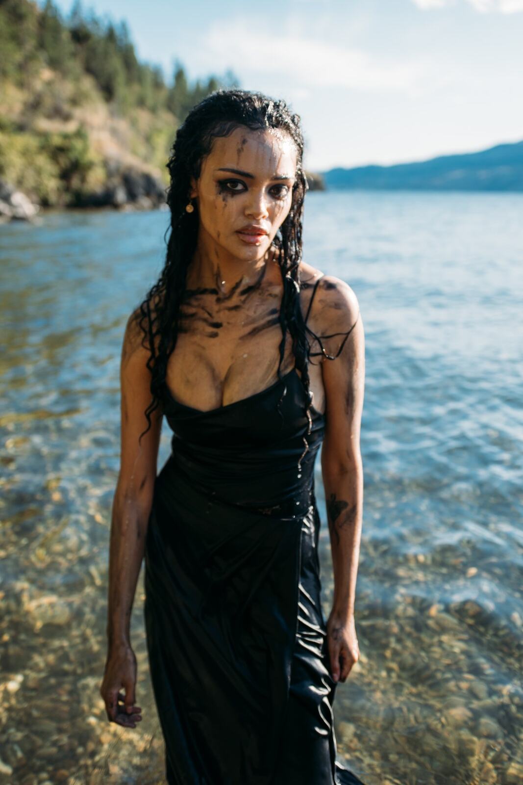 Alex by the Lake portraits story frame 7: Okanagan Lake portraits in Kelowna with black styling, rock, water, wind, direct expression and a cinematic beauty-portrait edge.