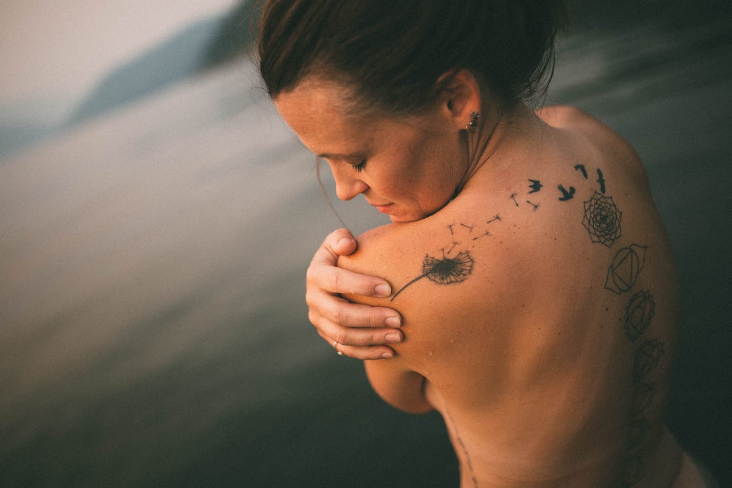 Erin at Mara Lake portraits story frame 12: Mara Lake portraits for Erin with driftwood, warm water, tattoo detail and soft evening light across the Shuswap shoreline.