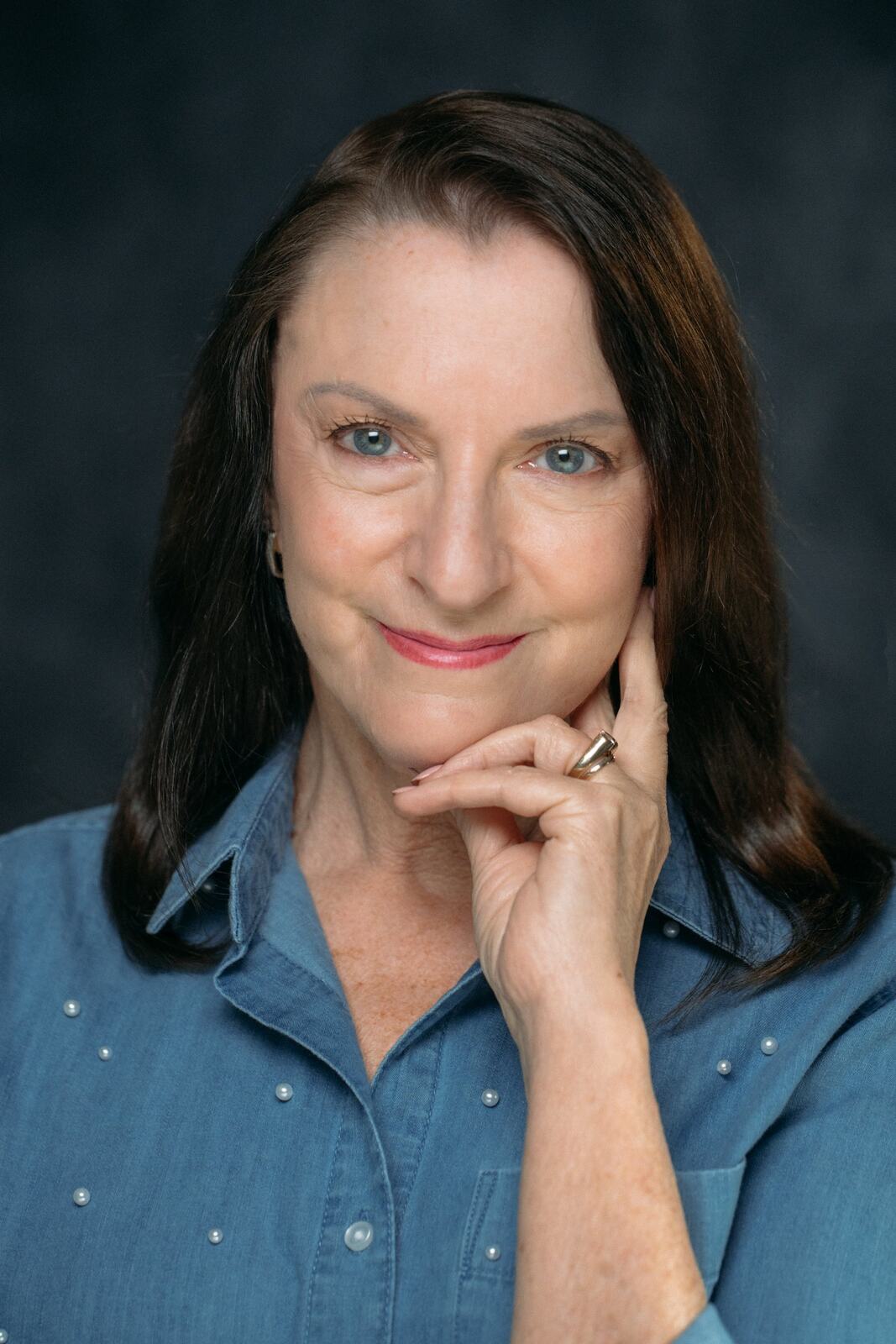 Marie smiling in a denim shirt with her hand near her chin