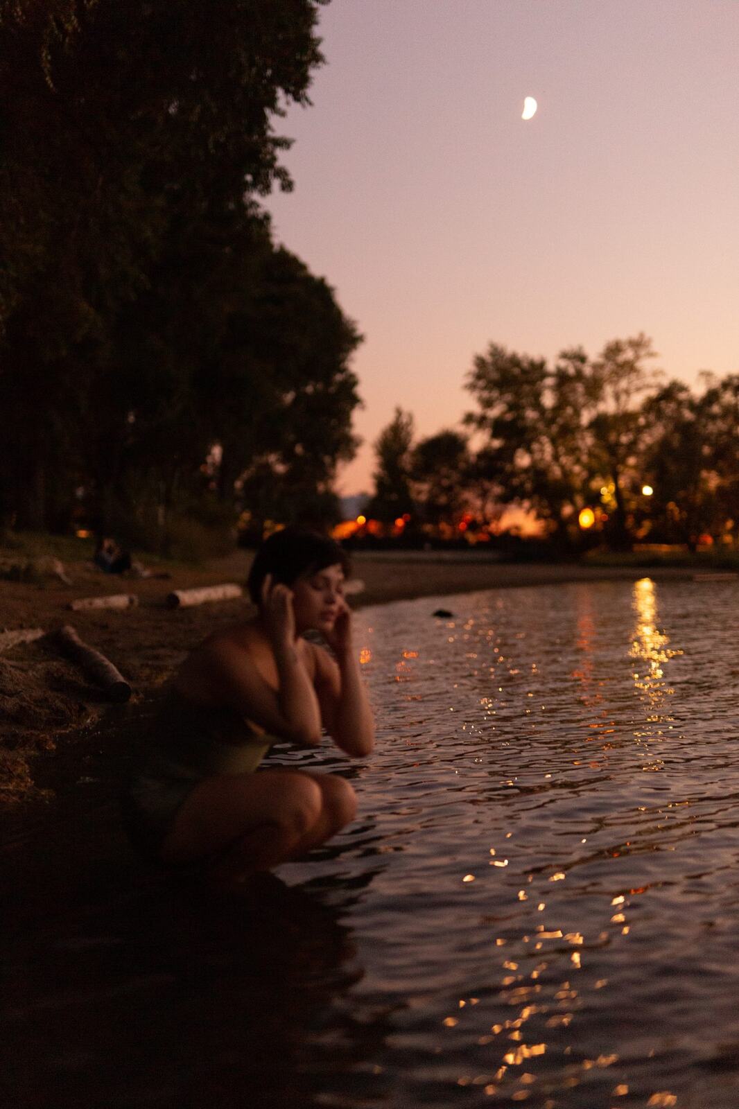 Lucy at the Water’s Edge portraits story frame 14: Lucy at the water’s edge as sunset slips into moonlight, moving from the shoreline and rocks to quiet close portraits and a warm-lit garden after dark. Photographed in Kelowna, BC.