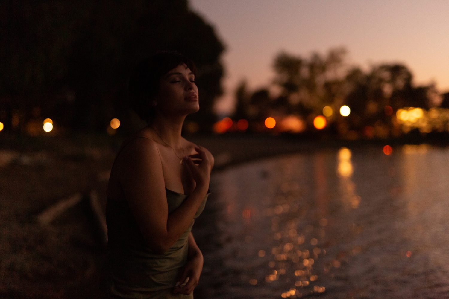Lucy at the Water’s Edge portraits story frame 19: Lucy at the water’s edge as sunset slips into moonlight, moving from the shoreline and rocks to quiet close portraits and a warm-lit garden after dark. Photographed in Kelowna, BC.