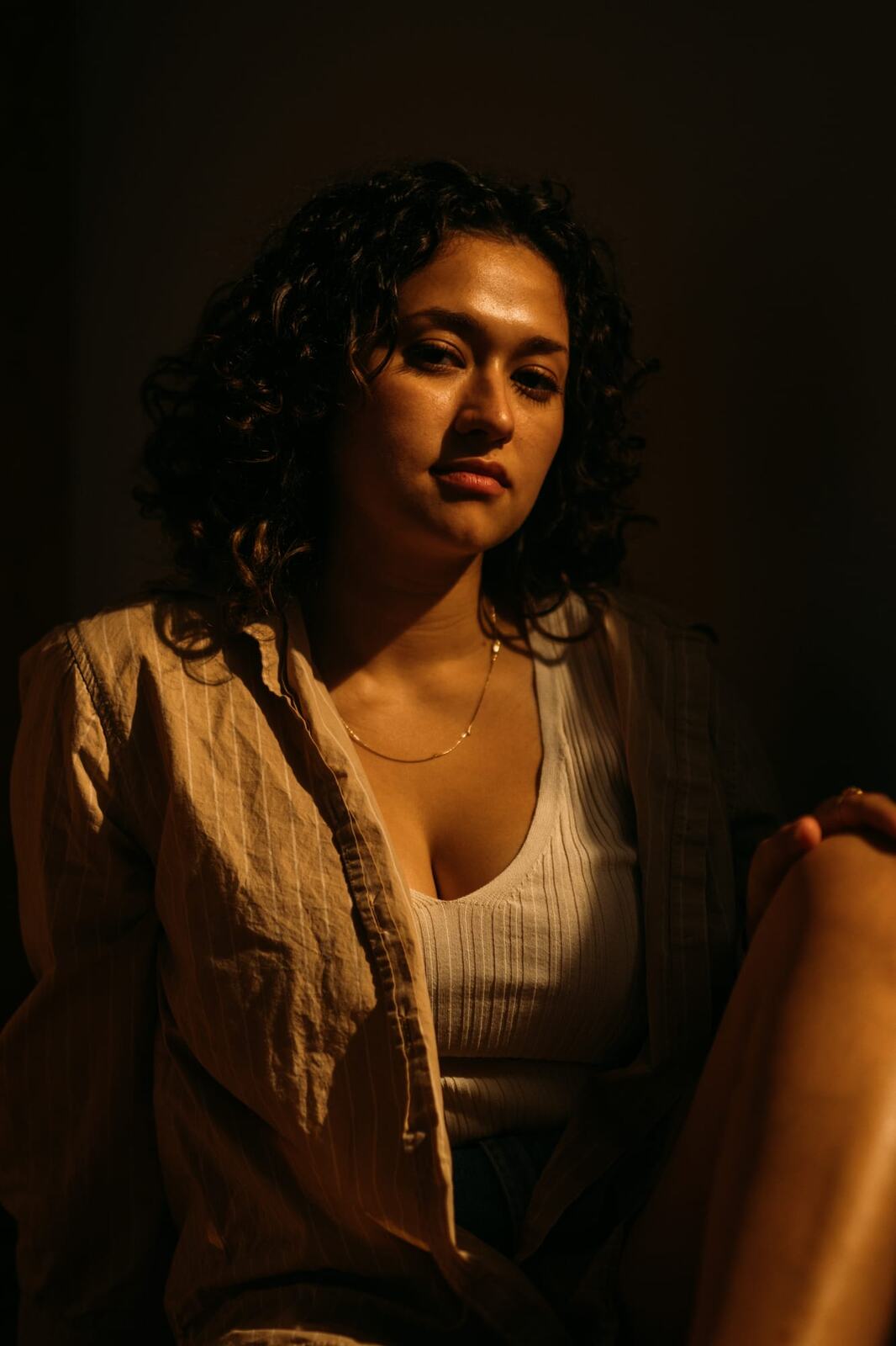 Marina in Warm Window Light portraits story frame 9: Marina in warm indoor light, with amber shadow, denim, black robe, green styling and an intimate editorial portrait mood.