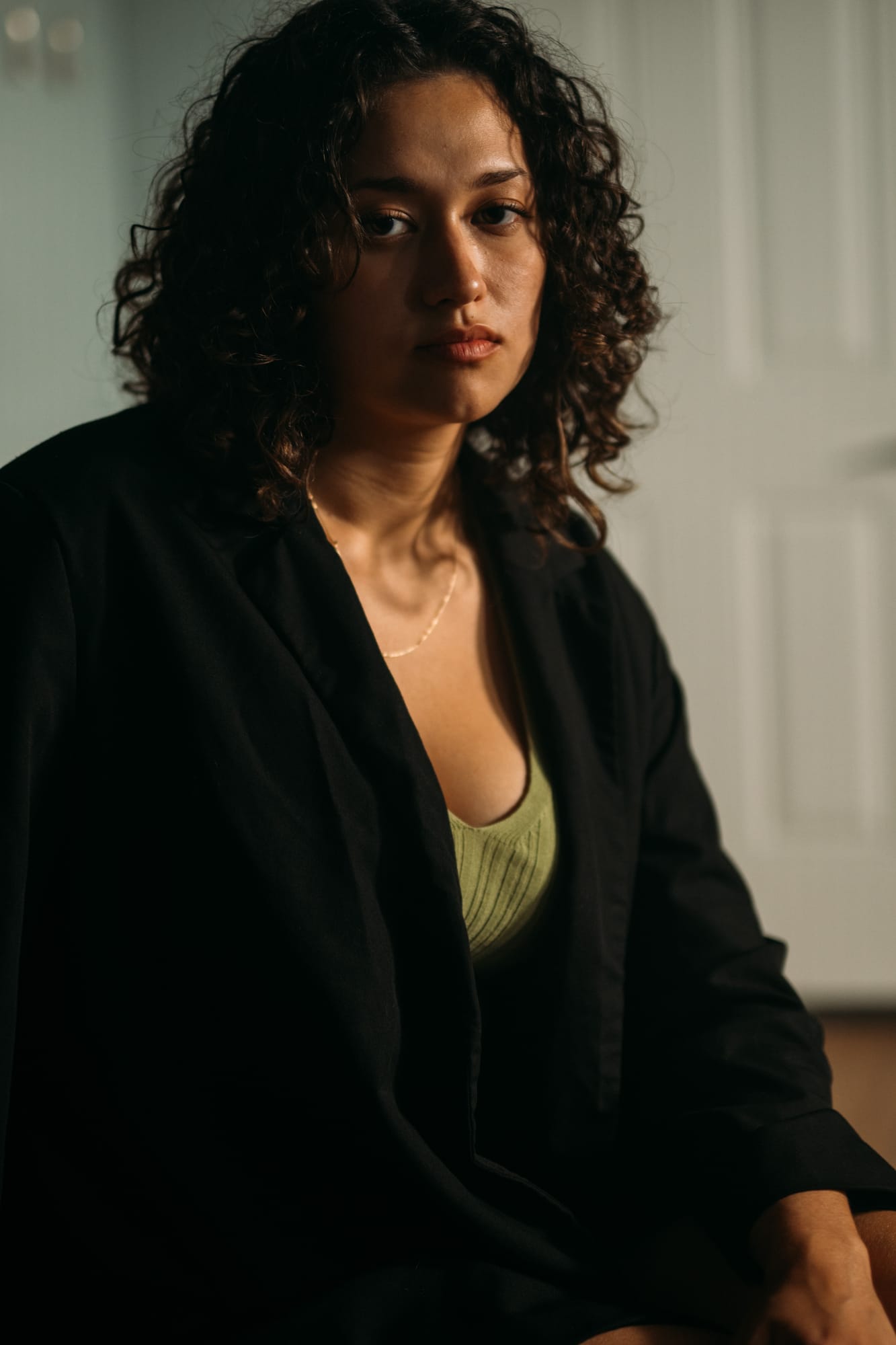 Marina in Warm Window Light portraits story frame 11: Marina in warm indoor light, with amber shadow, denim, black robe, green styling and an intimate editorial portrait mood.