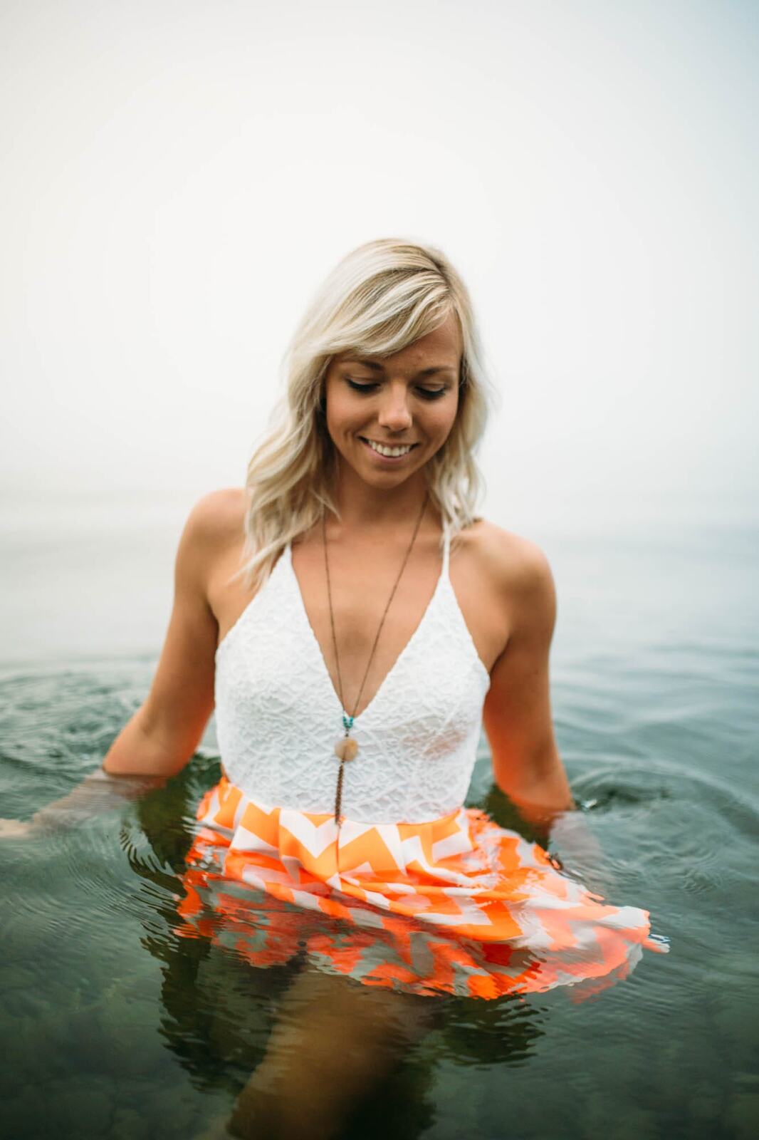 Megan Shallow portraits story frame 11: A fog-soft Kelowna lake portrait session for Megan Shallow, with water, orange dress movement, close body-language frames and quiet birds cutting through the mist.