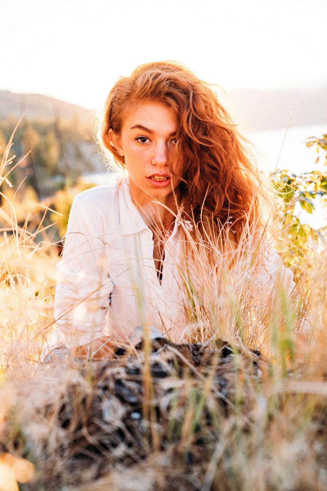 Mickie portraits story frame 4: A Kelowna portrait session for Mickie moving from golden grass and warm hillside light into lake-edge rocks, wind, white shirt styling and close editorial portraits.