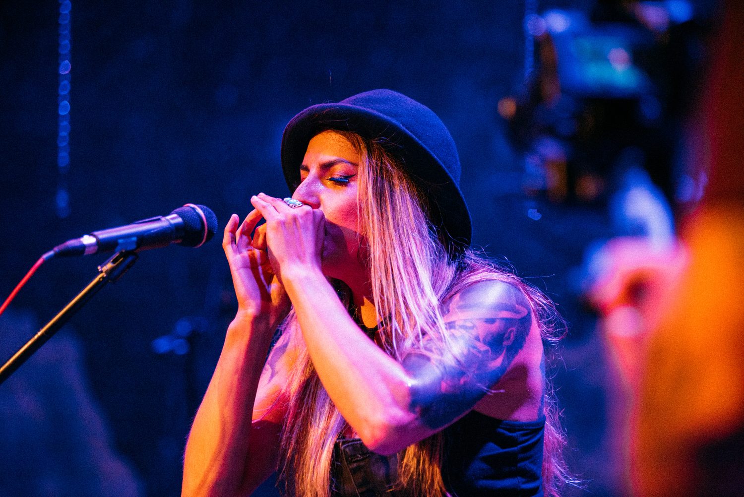Close singer-guitarist portrait with blue hat and cloud backdrop.