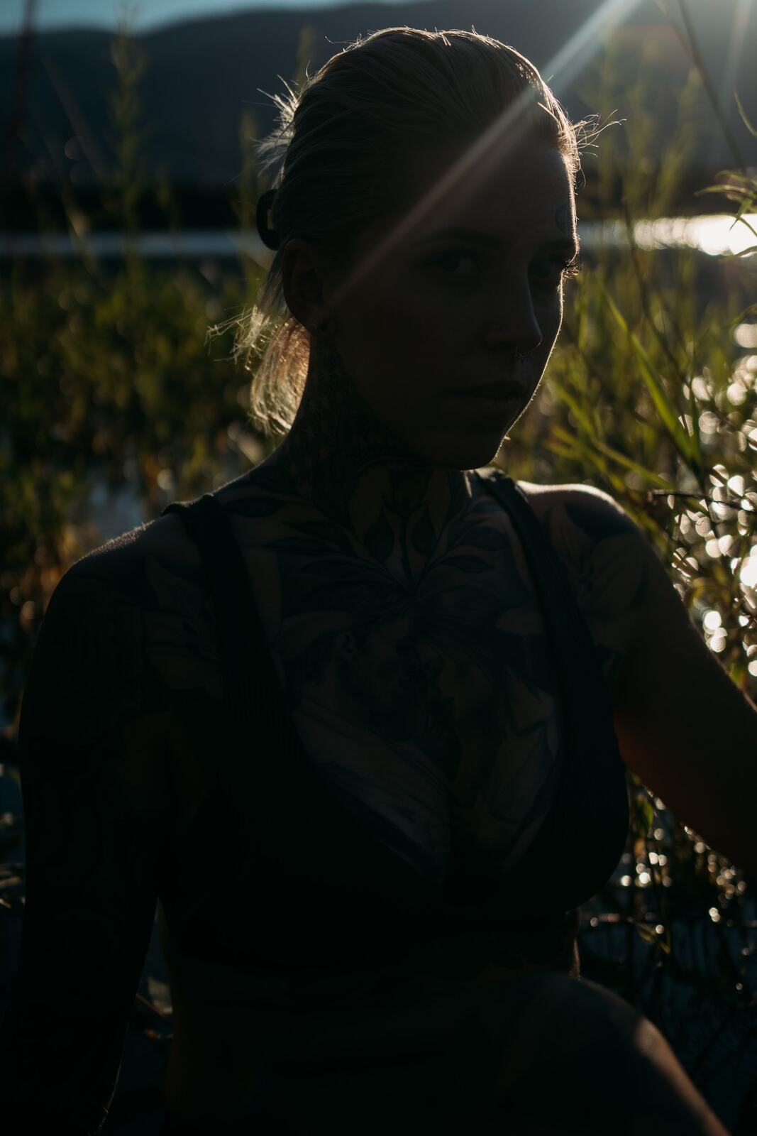 Rayleigh by Knox portraits story frame 11: Knox Mountain portraits in Kelowna with white floral dress, tattoo detail, reeds, water, sunlight and a stronger summer edge.