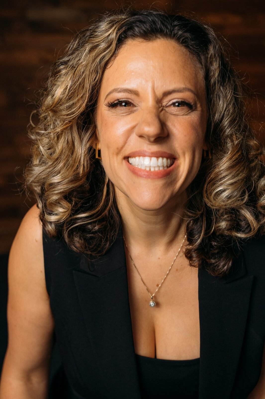 Trisha Miltimore corporate story frame 13: Personal-brand portraits for Trisha Miltimore in Kelowna, moving from clean business profile images into darker wood-wall portraits with black wardrobe and confident brand range..