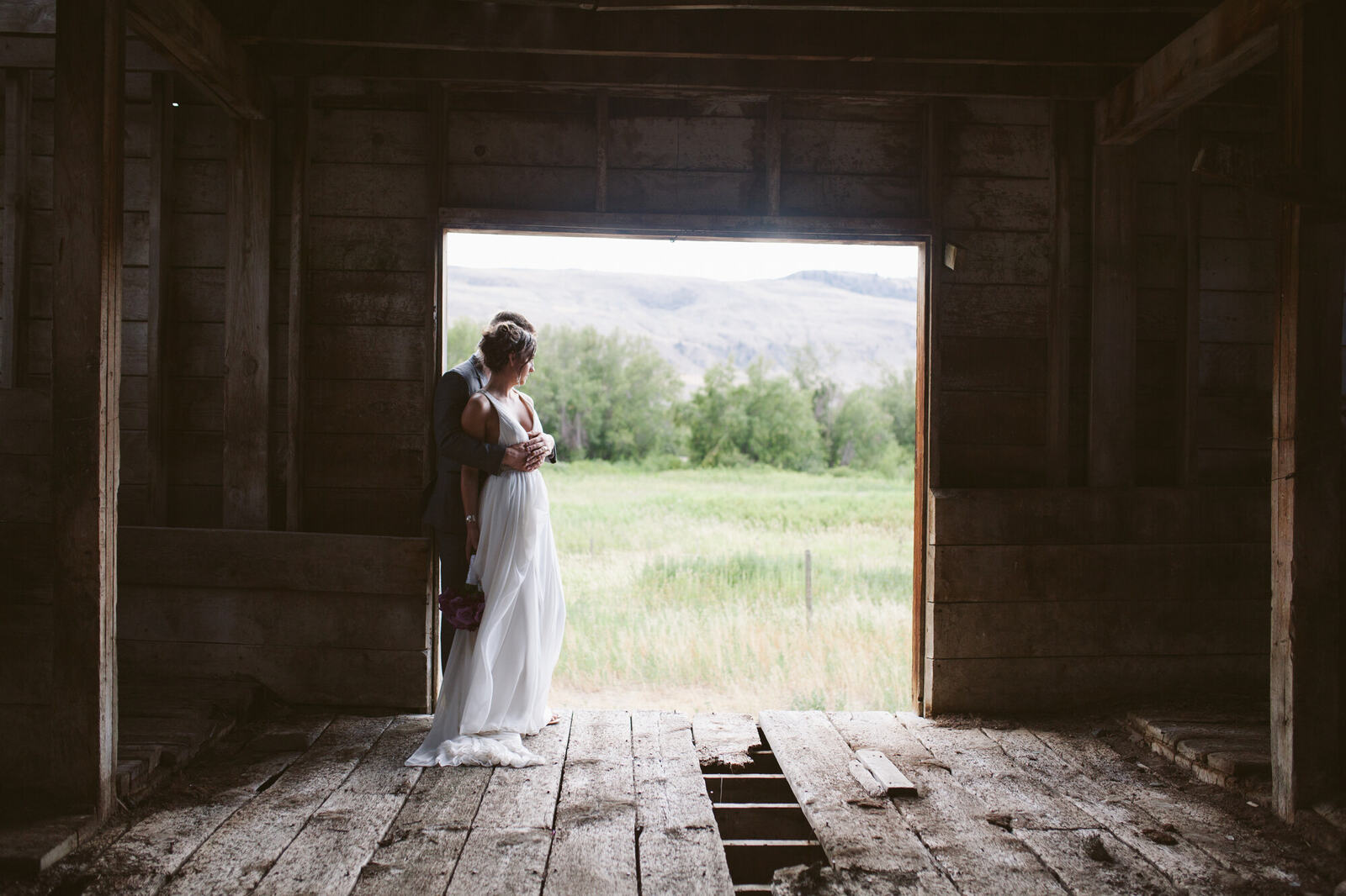 Becky standing inside a rustic doorway with open fields beyond at her Osoyoos wedding